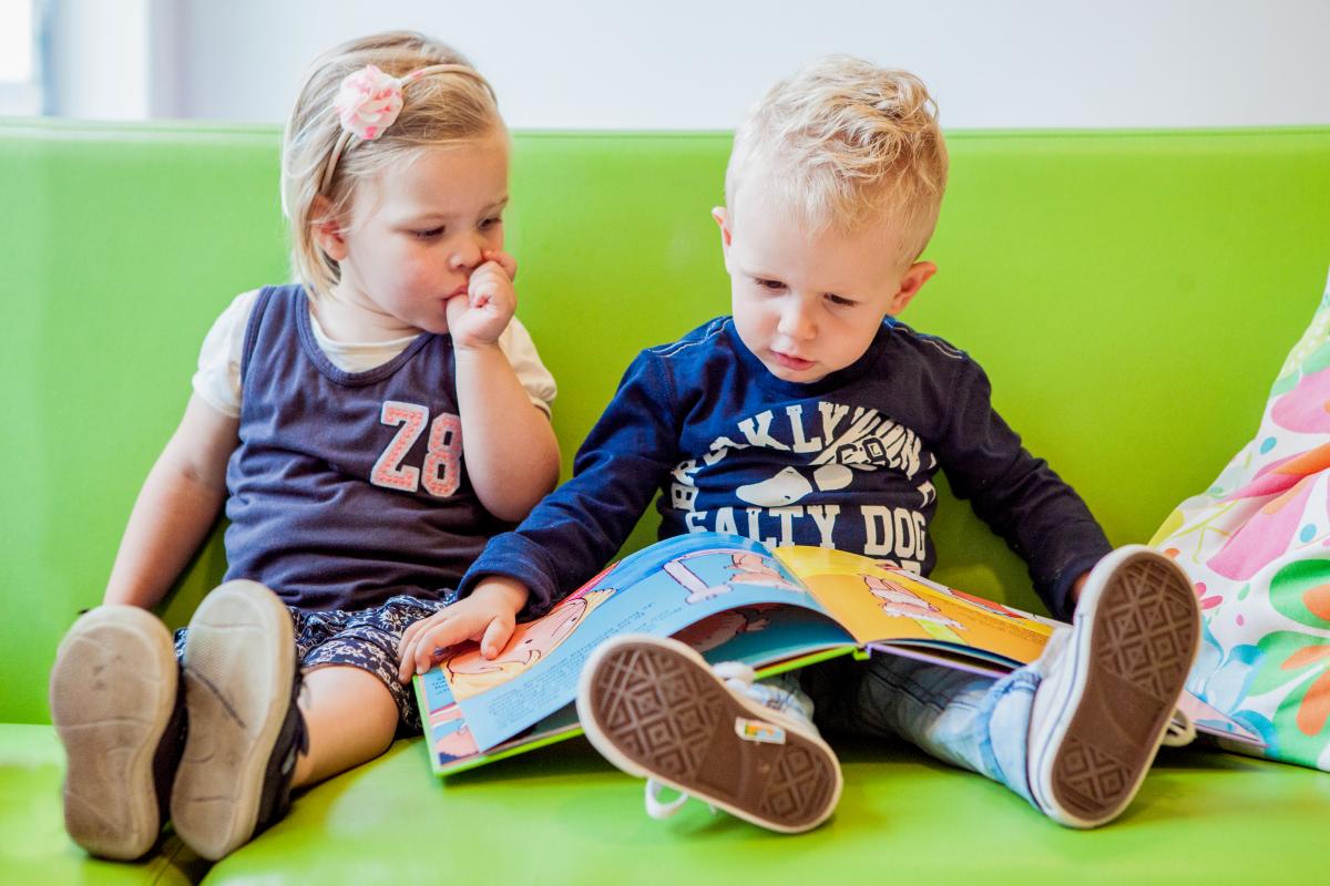 Een_meisje_en_jongen_lezen_samen_een_boek_op_de_bank_van_het_kinderdagverblijf